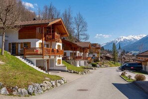 A row of traditional wooden houses with balconies, a clear sky, and a mountain range in the background. - Comfortable Alpine Chalet for 12 (Wald im Pinzgau)