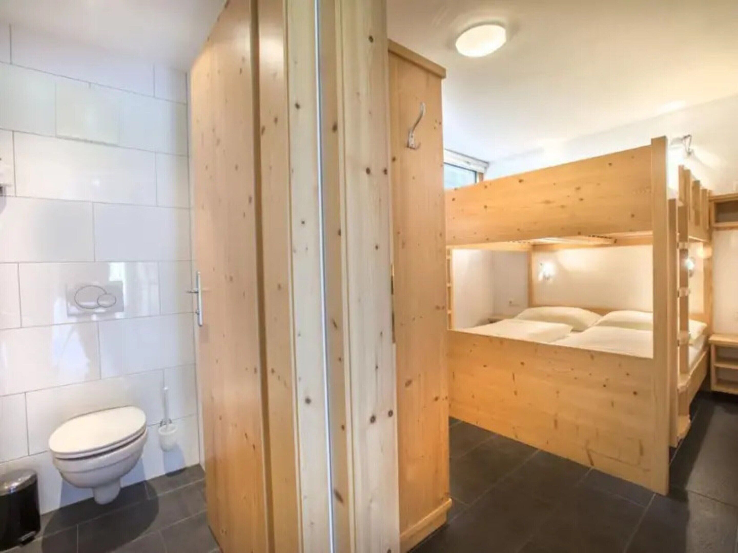 Une salle de bain équipée de toilettes, d’une douche et d’un lit superposé en bois avec un matelas.