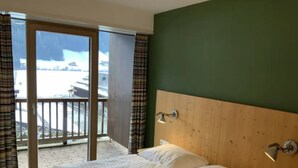 A hotel room with two beds, a wooden headboard, and a view of a snowy landscape through a sliding door. - Schoneben Mountain Holiday Home (Wald im Pinzgau)