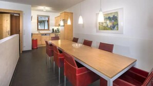 A modern kitchen with wooden cabinets, a dining table with red chairs, pendant lighting, and a framed artwork on the wall. - Schoneben Mountain Holiday Home (Wald im Pinzgau)