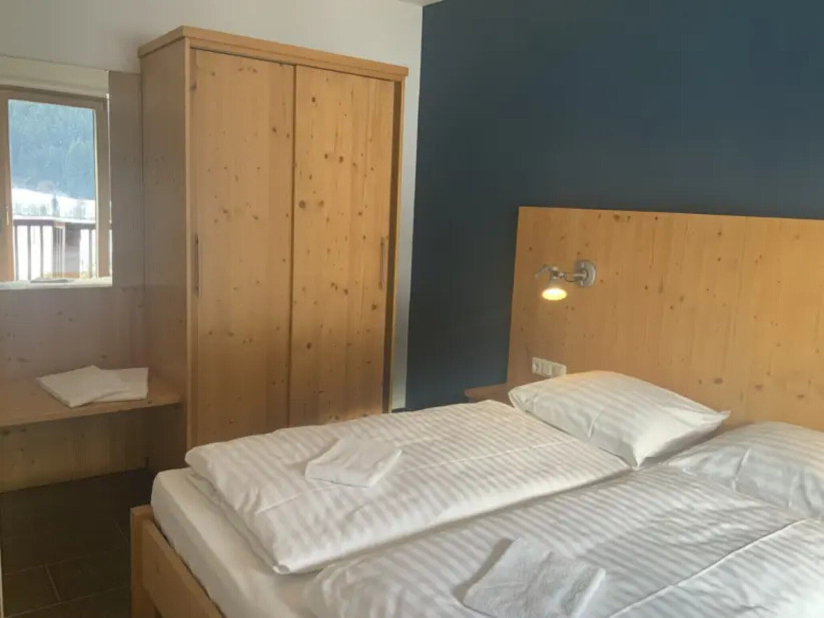 Un dormitorio con un armario de madera, una cama con ropa de cama blanca y una mesita de noche.