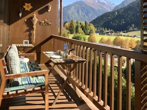 Um deck de madeira com mesa e cadeiras, com vista para uma paisagem montanhosa.