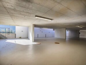 An empty parking garage with concrete floors and walls, numbered parking spots, and a visible staircase. - Schoneben Mountain Holiday Home (Wald im Pinzgau)