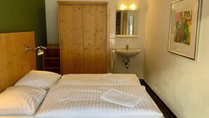 A hotel room with a bed, a wooden wardrobe, a bathroom with a sink and mirror, and a framed picture on the wall. - Schoneben Mountain Holiday Home (Wald im Pinzgau)