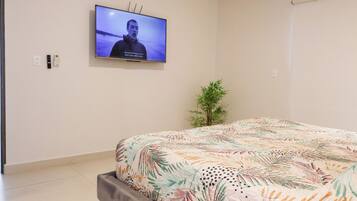 A bedroom with a bed, a television mounted on the wall, a small potted plant, and a window.