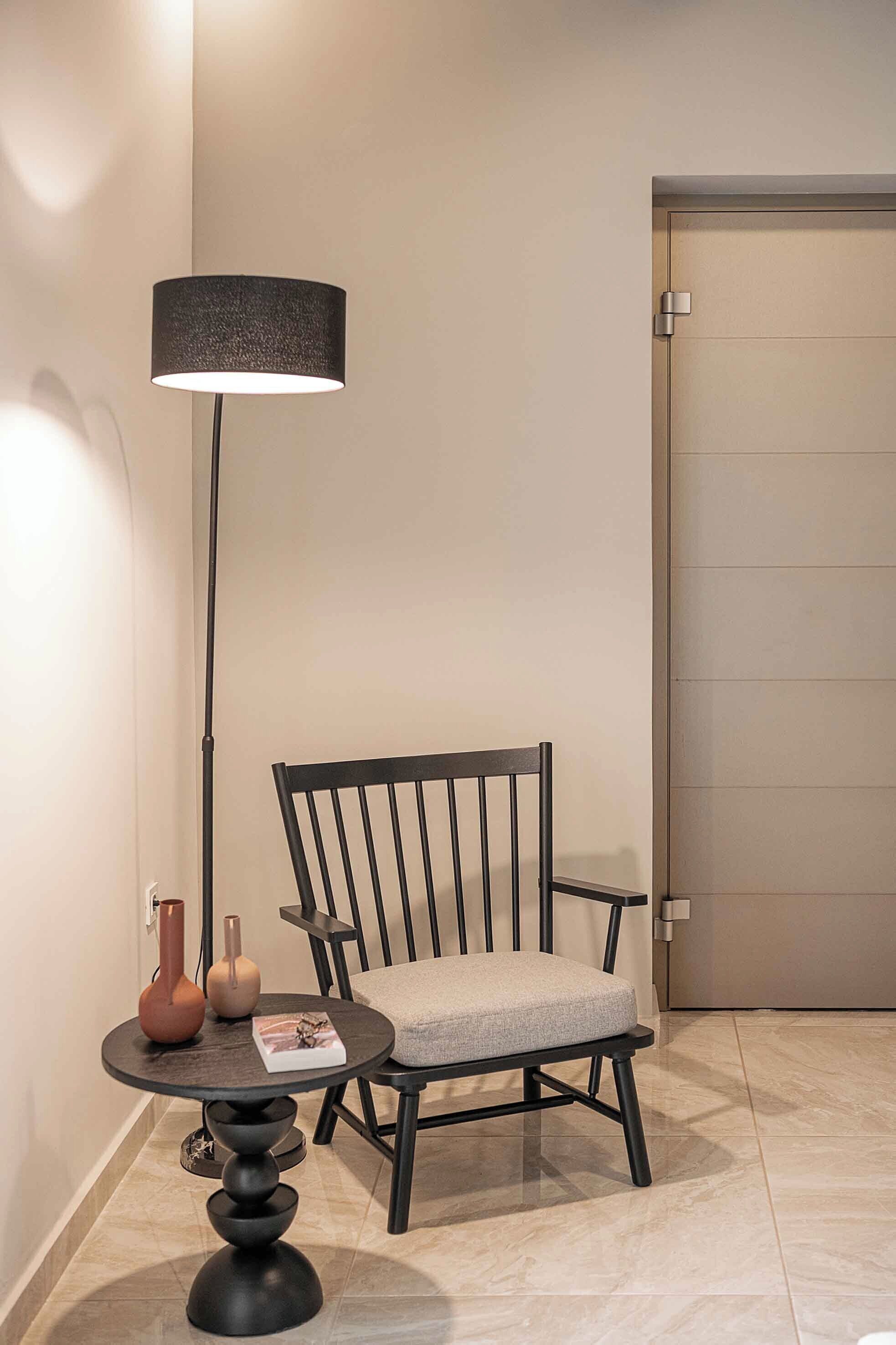 Et moderne værelse med en sort stol, et rundt bord med en lampe og to vaser.