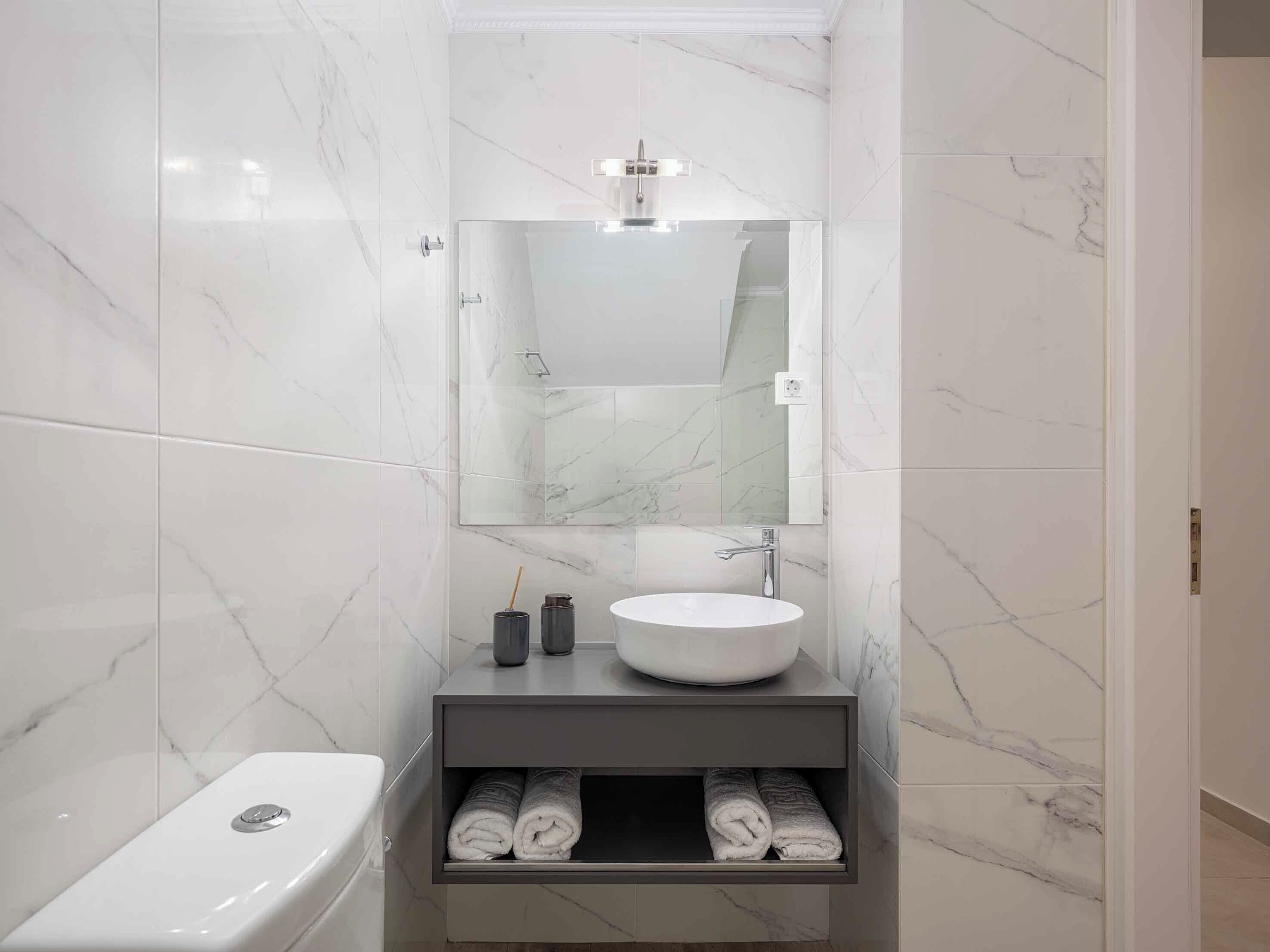 Une salle de bain moderne avec un lavabo en marbre blanc, un miroir au-dessus et un porte-serviettes avec des serviettes.