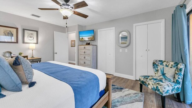 A bedroom with a bed, a ceiling fan, a dresser, a chair, and a television.