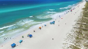 A beach with clear turquoise waters, a sandy shore, and several beach umbrellas and tents.