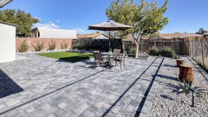 Un patio con una mesa y sillas, un árbol y un jardín cercado.
