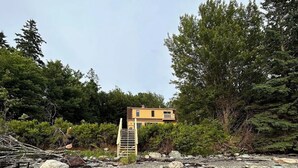 A small, two-story building with a balcony, surrounded by a rocky landscape and dense trees. - Bayberry  (Trenton)
