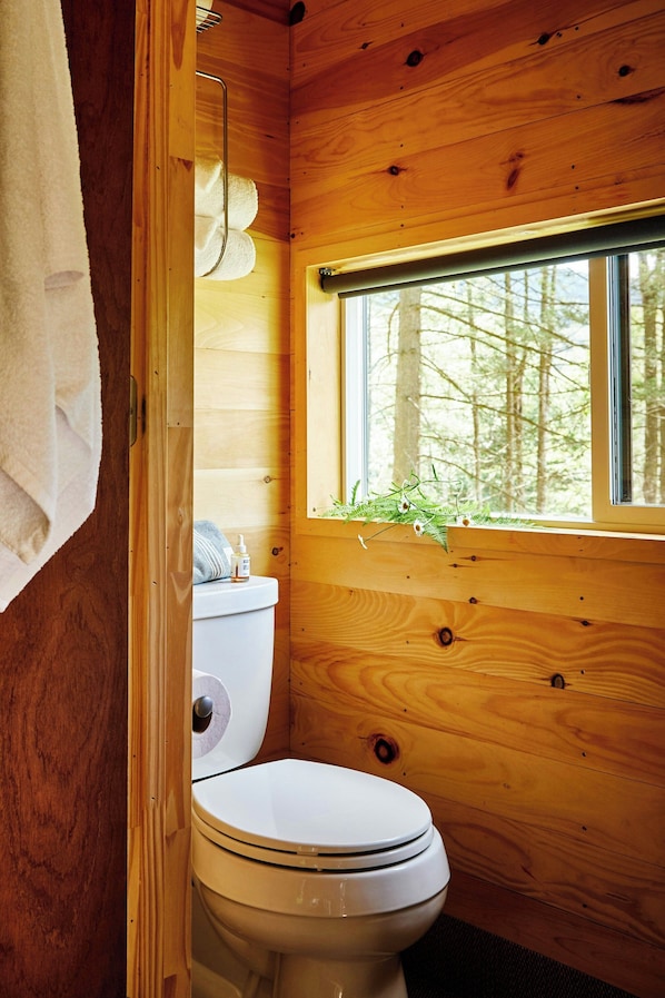 A wooden cabin bathroom with a toilet, a window with a view of trees, and a towel hanging on the wall. - Postcard Cabins Wild Rose, Outdoor Collection by Marriott Bonvoy (Wild Rose)