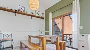 A dining area with a wooden table and benches, a hanging light fixture, and a view of the outside balcony.