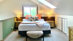 A bedroom with a large bed, two bedside tables, a bench, a window, and a skylight.