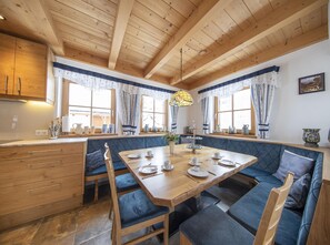 A cozy dining area with a wooden table and blue upholstered benches, wooden cabinets, and a stained glass pendant light. - Family Alpine Chalet in Wald im Pinzgau (Wald im Pinzgau)