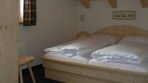 Una cama individual con cabecera de madera en una habitación con techos inclinados y un taburete pequeño.