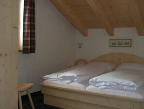 A single bed with a wooden headboard in a room with sloped ceilings and a small stool. - Sunlit Alpine Chalet Stay (Wald im Pinzgau)