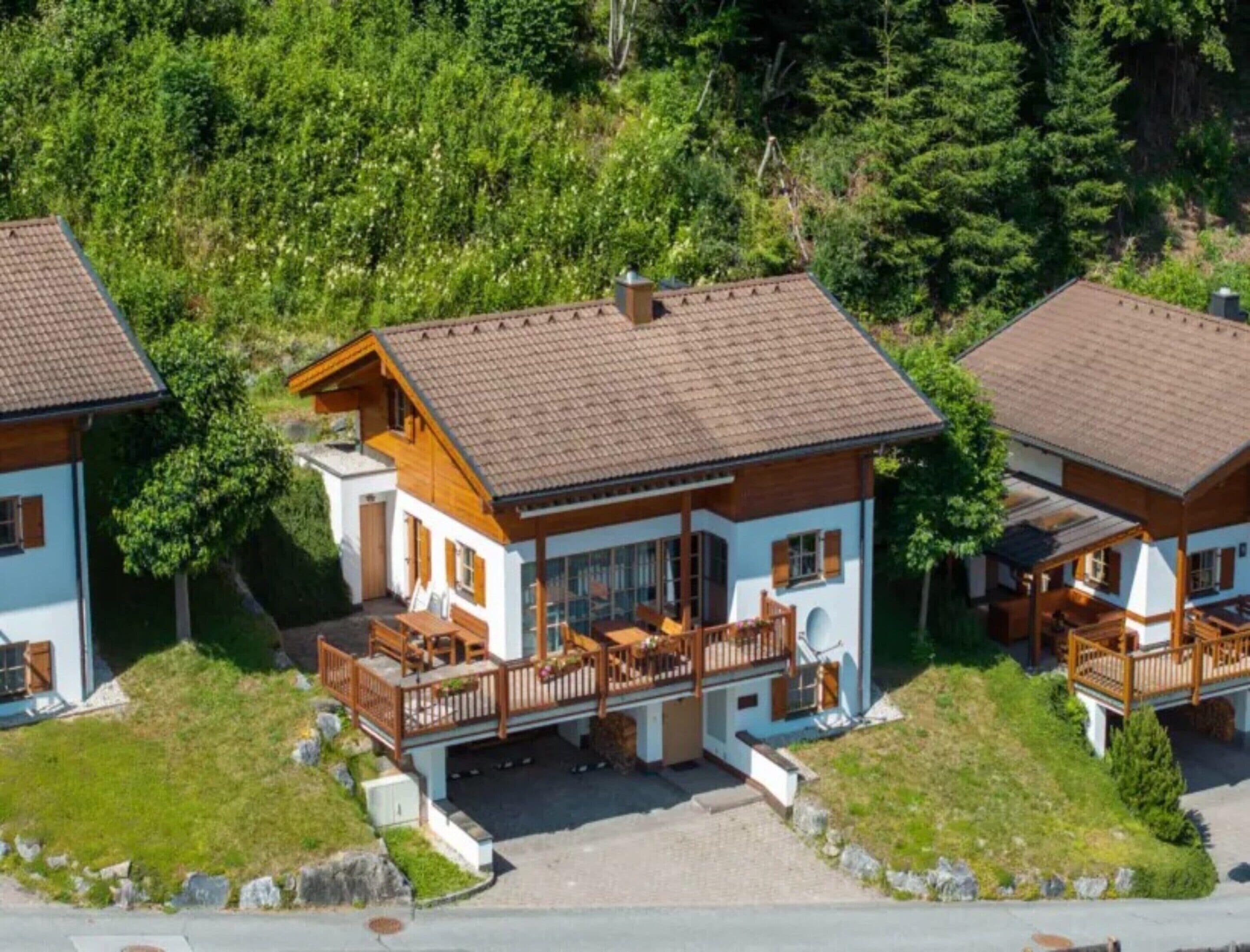 A two-story chalet with a balcony, surrounded by greenery.