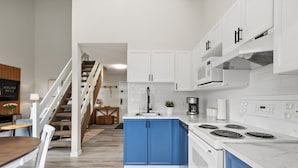 Une cuisine moderne avec des armoires blanches, des touches de bleu, une cuisinière intégrée et un coin repas comprenant une table et des chaises en bois.