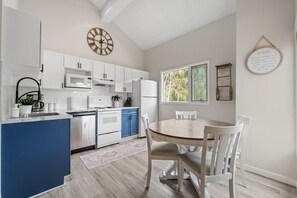 Una cocina moderna con gabinetes blancos, una isla azul, electrodomésticos de acero inoxidable y un comedor con sillas blancas.