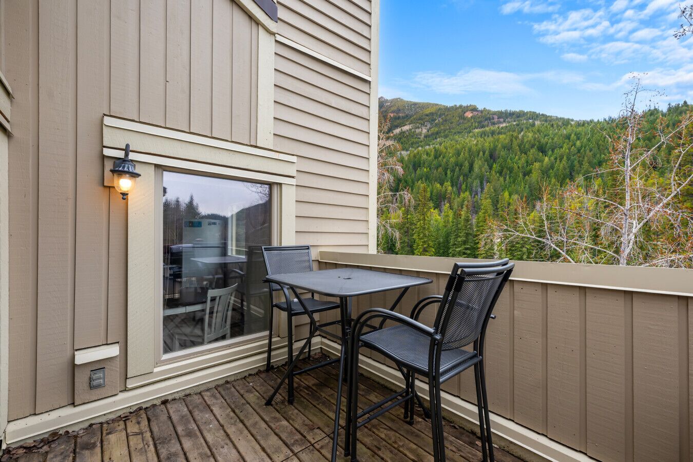 Un balcon avec une table et des chaises, une fenêtre et une vue sur une colline boisée.