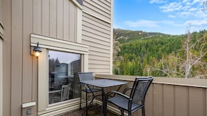 Un balcon avec une table et des chaises, une fenêtre et une vue sur une colline boisée.