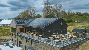 A building with a stone facade, a flat roof with solar panels, and an outdoor seating area with tables and chairs. - Meadow House at Seminary Hill by Avantstay (Callicoon)
