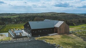 A large barn with a sloped roof, a covered outdoor seating area with tables and chairs, and a paved driveway leading to the entrance. - Meadow House at Seminary Hill by Avantstay (Callicoon)