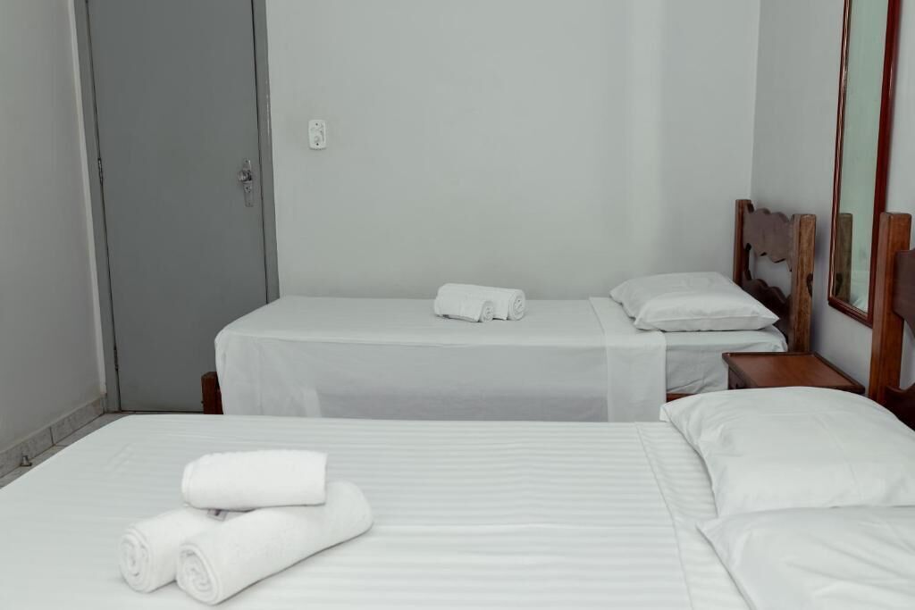 A hotel room with two single beds, each with white linens and pillows, a wooden headboard, and a small bedside table.