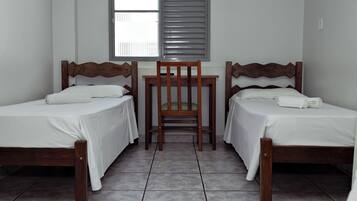 Een kamer met twee houten bedden, een klein tafeltje en een raam met rolluiken.