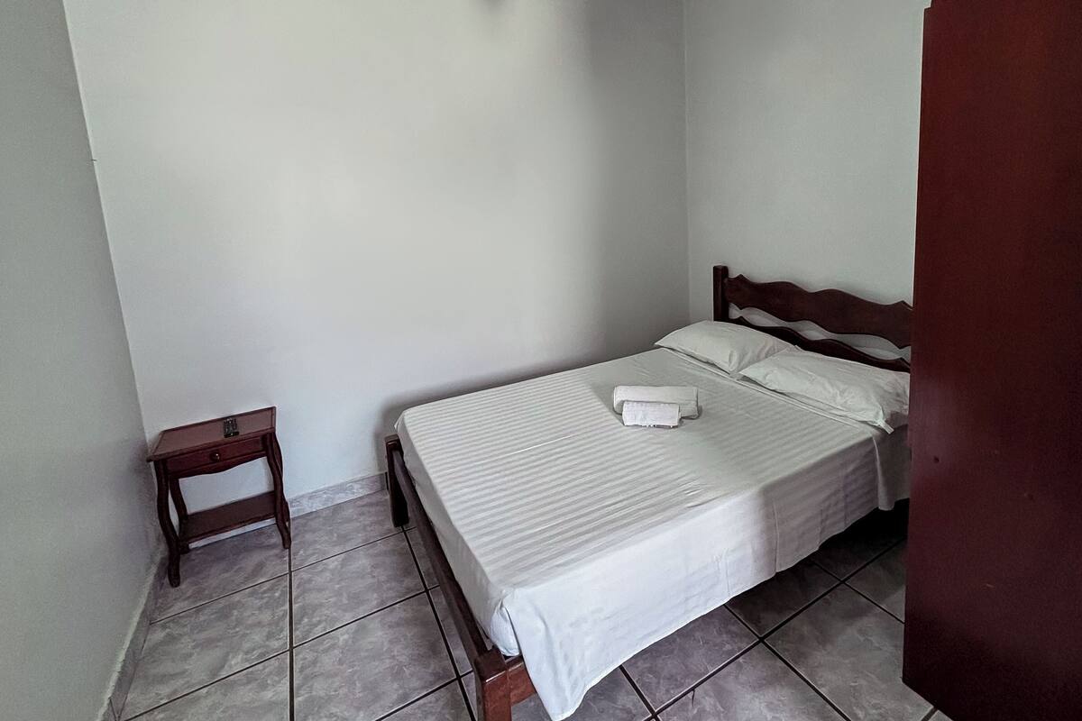 A small, clean room with a single bed, a wooden nightstand, and a door.
