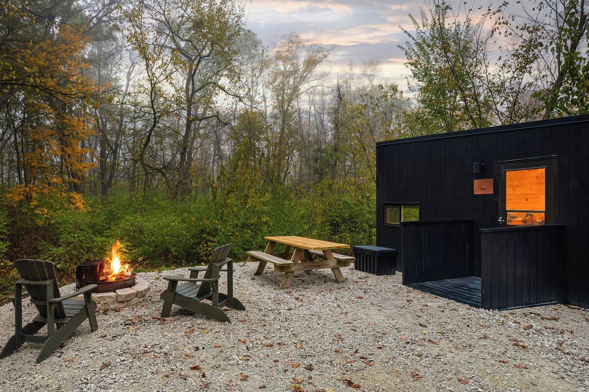 A rustic cabin with a fire pit and seating area surrounded by trees.