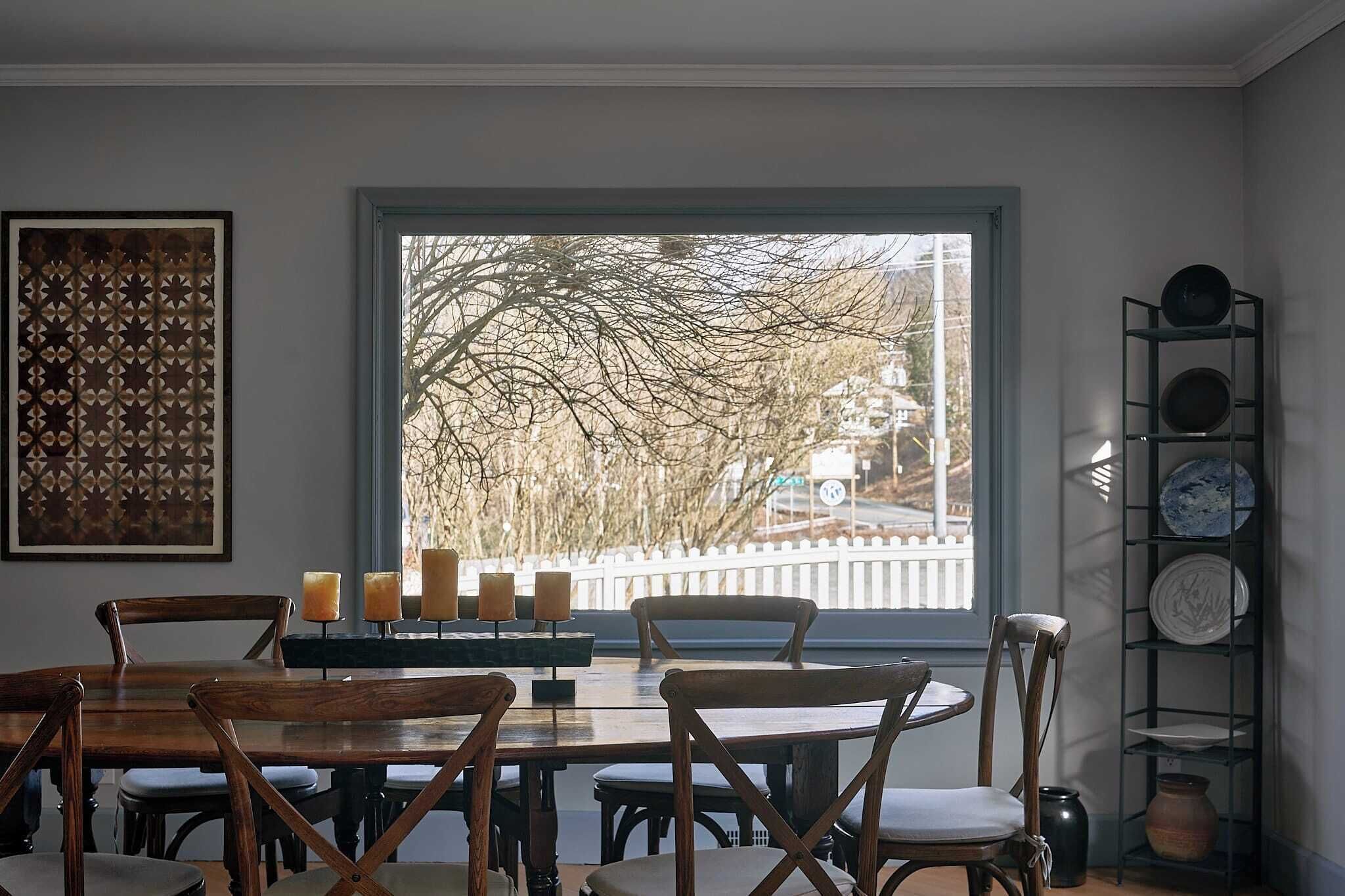 A dining area with a large window, wooden chairs, a table, and a candle holder with candles.