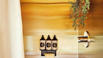 Zona de ducha con techo de madera, una planta colgante y tres botellas de champú.