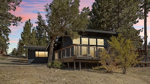 A modern cabin with a deck, surrounded by trees, and a small attached structure. - YOLO Lake Escape | Lakefront Views - EV Charger (Big Bear Lake)