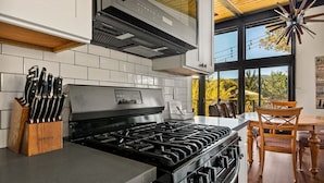 A modern kitchen with a gas stove, knife block, and a dining area with a wooden table and chairs. - YOLO Lake Escape | Lakefront Views - EV Charger (Big Bear Lake)
