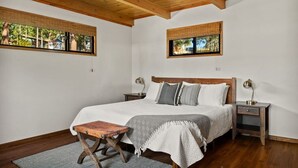 A bedroom with a wooden ceiling, a bed with a headboard, bedside tables, a nightstand, and a window with a view. - YOLO Lake Escape | Lakefront Views - EV Charger (Big Bear Lake)