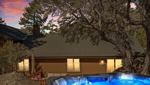 A hot tub in front of a wooden cabin with a view of a tree and a sunset. - Enchanting Escape | Hot Tub, Fire Pit & Game Room (Big Bear Lake)