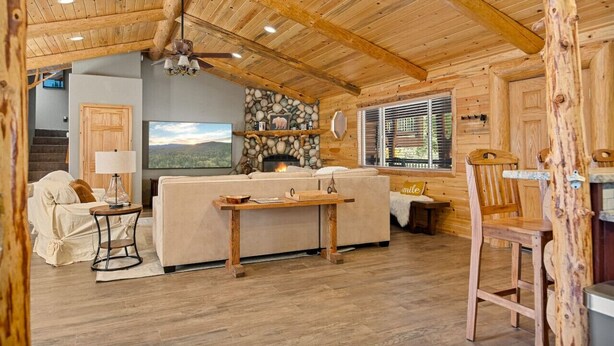 A cozy log cabin interior with a stone fireplace, a large flat-screen TV, and a wooden ceiling. - Enchanting Escape | Hot Tub, Fire Pit & Game Room (Big Bear Lake)