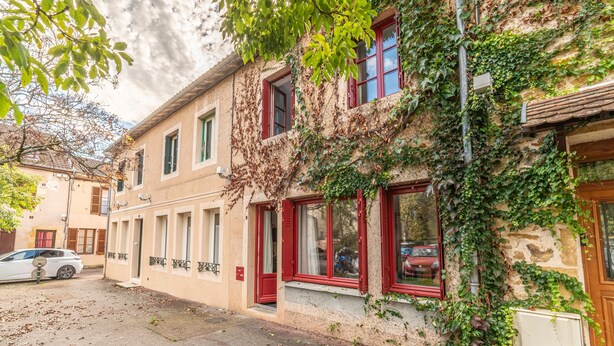Un edificio de fachada de piedra, contraventanas rojas y enredaderas.