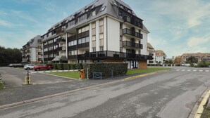 A multi-story residential building with balconies, a gated entrance, and a parking area. - L'Estran - Appt 2p, proche de la mer (Villers-sur-Mer)