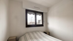 A bedroom with a bed, a window, a nightstand, and a wall-mounted air conditioner. - L'Estran - Appt 2p, proche de la mer (Villers-sur-Mer)