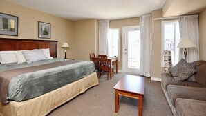 Ein Hotelzimmer mit Bett, Schreibtisch, Stuhl, Sofa und einer Tür, die auf einen Balkon führt.