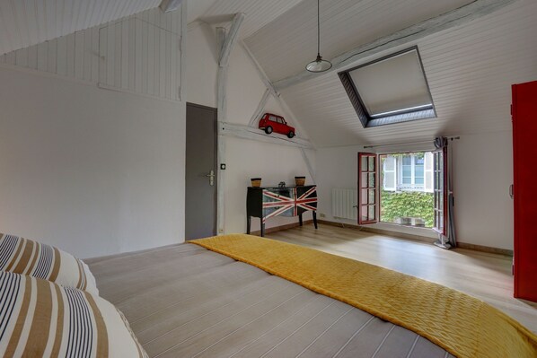 A spacious room with a high ceiling, a skylight, a bed with striped bedding, a yellow rug, a small table with a Union Jack flag, and a red car model on the ceiling. - Le Rabelais - Appt, à 5min du château d'Amboise (Amboise)