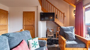 A cozy living room with a wooden staircase, a flat-screen TV, and a sofa with decorative pillows.