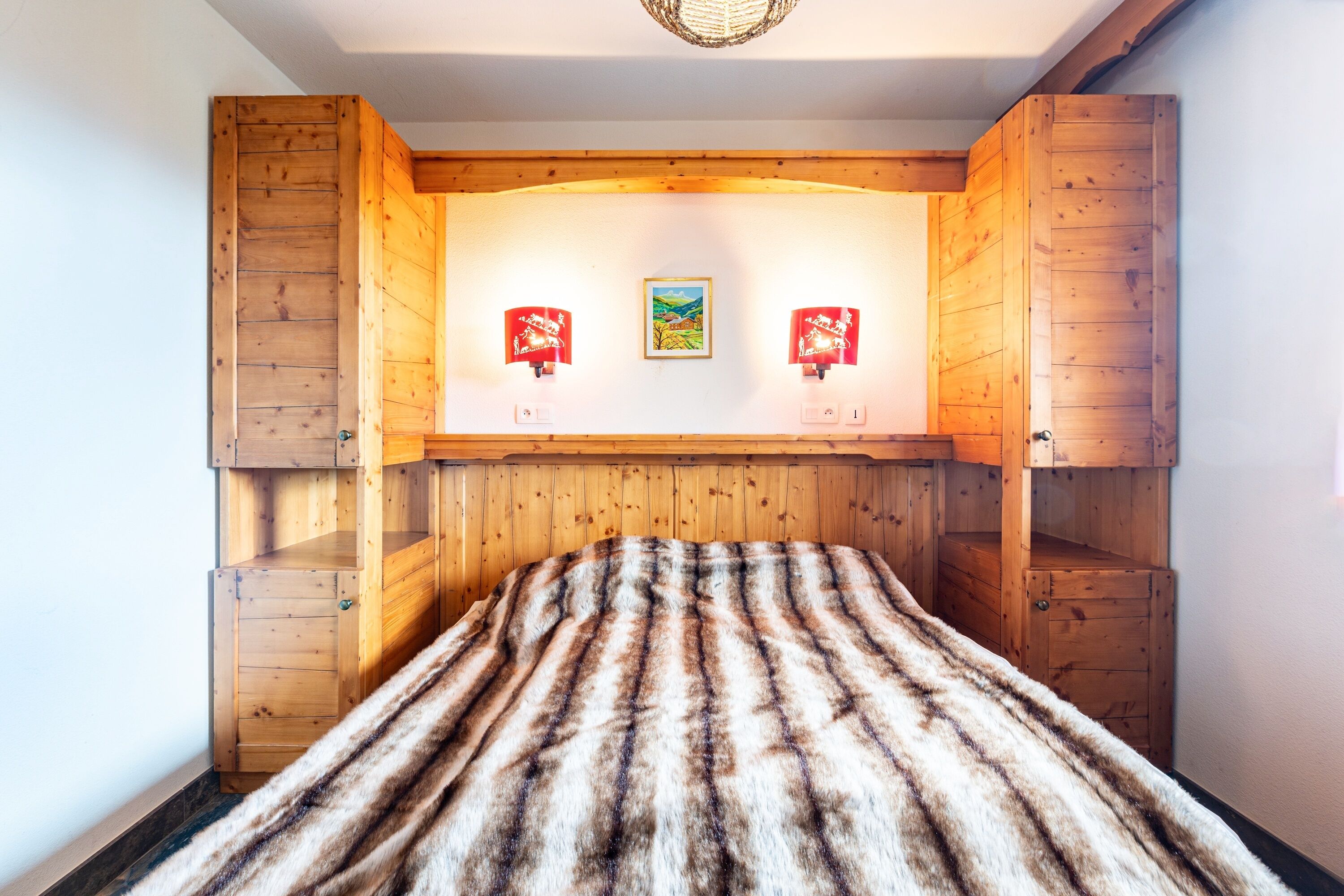 A room with a wooden headboard, a fur-covered bed, and two wall-mounted lamps.