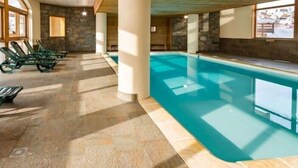 An indoor swimming pool with clear water, surrounded by stone walls and wooden beams.