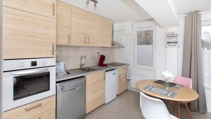 Una cocina compacta con gabinetes de madera, horno empotrado, lavavajillas y un pequeño comedor con mesa y sillas.