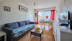 Un salon moderne comprenant un canapé, une table basse avec des fruits, un téléviseur et un coin repas avec une table et des chaises.