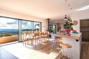 A modern kitchen with a large island, wooden flooring, and a view of the outdoors. - Maison Altea - Maison climatisée (Figari)